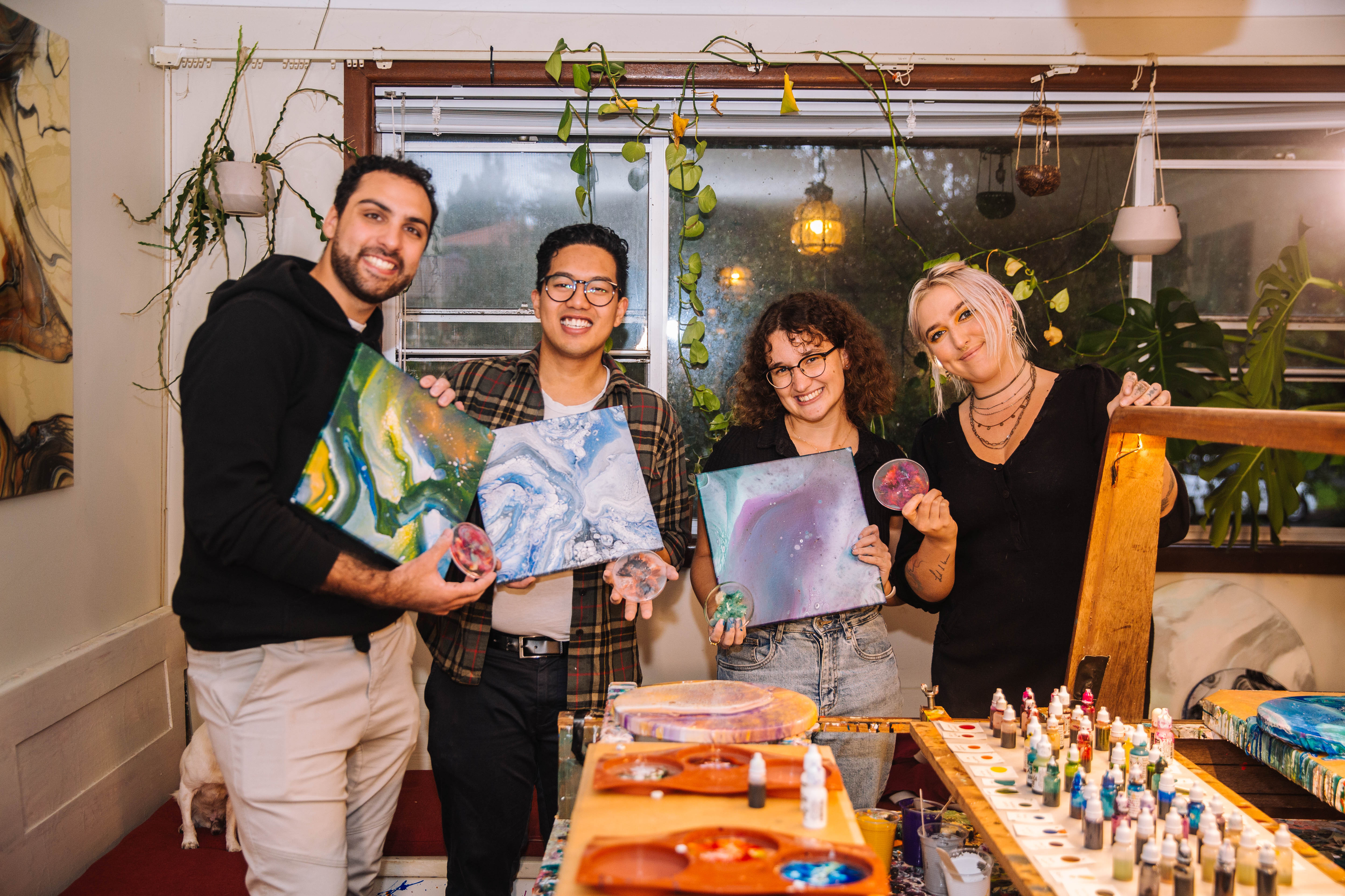 Group of four smiling people holding up fluid artworks